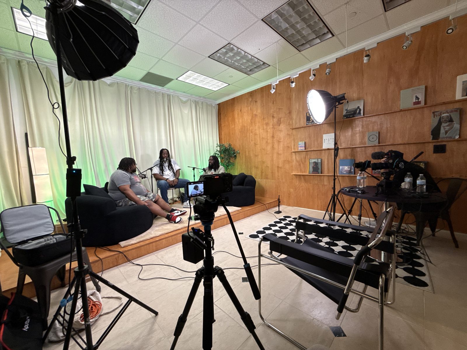 Three-person podcast set lit with softboxes, cameras on tripods in the foreground